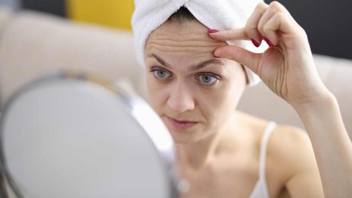 une femme examine les rides de son front dans le miroir