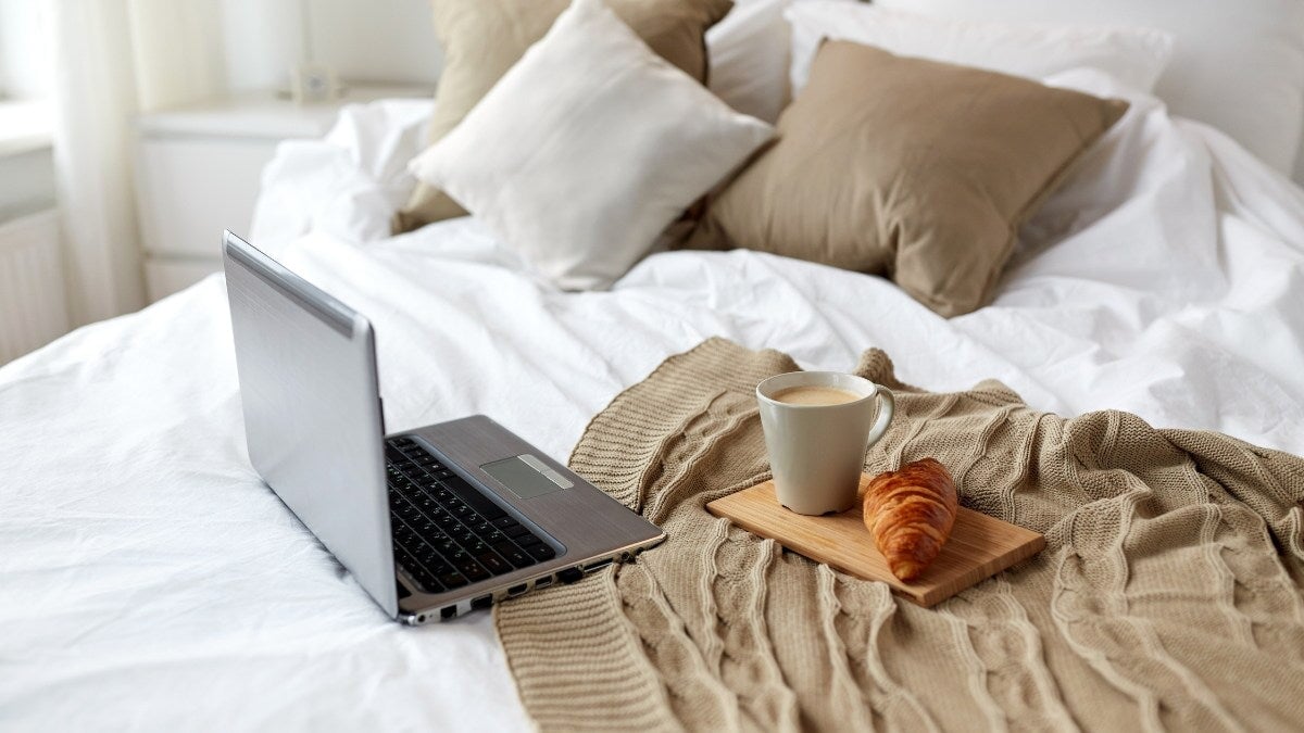 une tasse de thé, un croissant et un ordinateur portable sur un lit