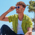 Lucas regarde au loin avec ses lunettes Stockholm solaires assis sur un muret sous le soleil et un arbre